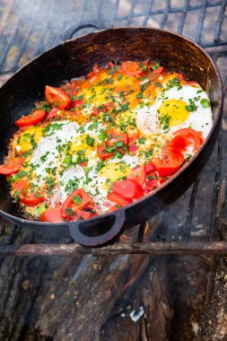 Yumurtalar, ormanda ateşte tavada sebzelerle hazırlandı. Açık ateşte çırpılmış yumurta pişirmek. Doğada kahvaltı. Turist yemeği..
