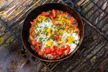 Yumurtalar, ormanda ateşte tavada sebzelerle hazırlandı. Açık ateşte çırpılmış yumurta pişirmek. Doğada kahvaltı. Turist yemeği..