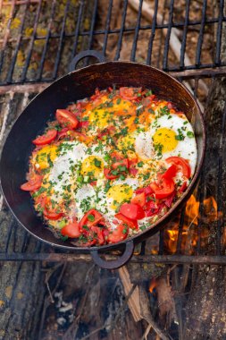 Yumurtalar, ormanda ateşte tavada sebzelerle hazırlandı. Açık ateşte çırpılmış yumurta pişirmek. Doğada kahvaltı. Turist yemeği..