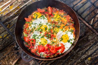 Yumurtalar, ormanda ateşte tavada sebzelerle hazırlandı. Açık ateşte çırpılmış yumurta pişirmek. Doğada kahvaltı. Turist yemeği..