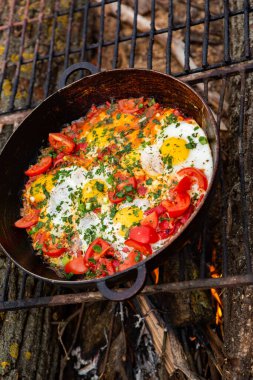 Yumurtalar, ormanda ateşte tavada sebzelerle hazırlandı. Açık ateşte çırpılmış yumurta pişirmek. Doğada kahvaltı. Turist yemeği..