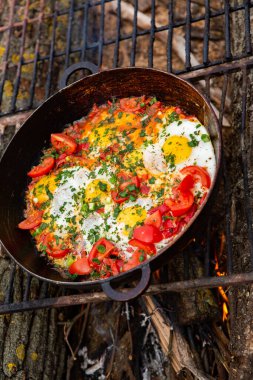 Yumurtalar, ormanda ateşte tavada sebzelerle hazırlandı. Açık ateşte çırpılmış yumurta pişirmek. Doğada kahvaltı. Turist yemeği..