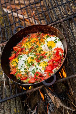 Yumurtalar, ormanda ateşte tavada sebzelerle hazırlandı. Açık ateşte çırpılmış yumurta pişirmek. Doğada kahvaltı. Turist yemeği..