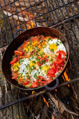 Yumurtalar, ormanda ateşte tavada sebzelerle hazırlandı. Açık ateşte çırpılmış yumurta pişirmek. Doğada kahvaltı. Turist yemeği..