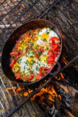 Yumurtalar, ormanda ateşte tavada sebzelerle hazırlandı. Açık ateşte çırpılmış yumurta pişirmek. Doğada kahvaltı. Turist yemeği..