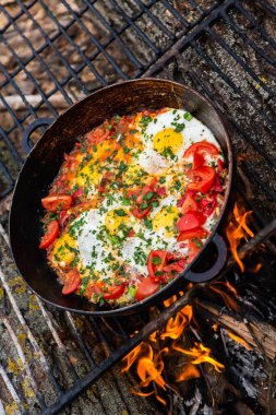 Yumurtalar, ormanda ateşte tavada sebzelerle hazırlandı. Açık ateşte çırpılmış yumurta pişirmek. Doğada kahvaltı. Turist yemeği..