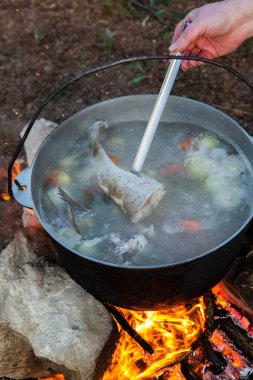 Açık ateşte hazırlanmış balık çorbası. Çaydanlıkta açık ateşte balık çorbası pişirmek. Turizm ve balıkçılıkta yemek pişirmek