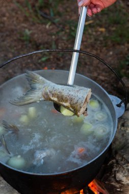 Açık ateşte hazırlanmış balık çorbası. Çaydanlıkta açık ateşte balık çorbası pişirmek. Turizm ve balıkçılıkta yemek pişirmek