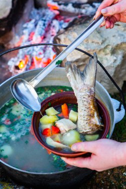 Açık ateşte hazırlanmış balık çorbası. Çaydanlıkta açık ateşte balık çorbası pişirmek. Turizm ve balıkçılıkta yemek pişirmek