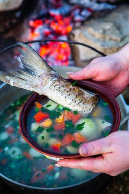 Açık ateşte hazırlanmış balık çorbası. Çaydanlıkta açık ateşte balık çorbası pişirmek. Turizm ve balıkçılıkta yemek pişirmek