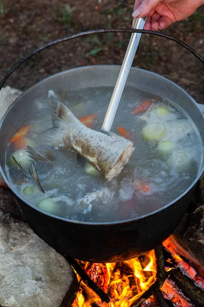 Fish soup prepared over an open fire. Cooking fish soup over an open fire in a kettle. Cooking in hiking tourism and fishing