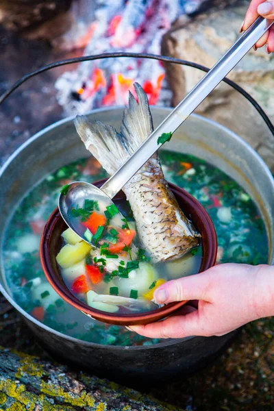 Açık ateşte hazırlanmış balık çorbası. Çaydanlıkta açık ateşte balık çorbası pişirmek. Turizm ve balıkçılıkta yemek pişirmek
