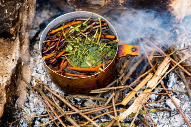 Vahşi doğada hayatta kalmak. Kamp ateşi arka planı. Ateşin üstünde vişneli çay çubuklarıyla tava. Vahşi doğada çay pişirmek....