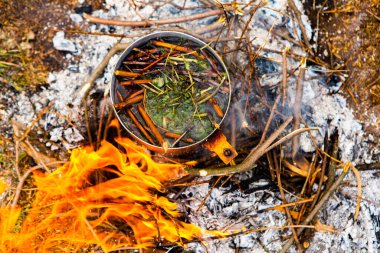 Vahşi doğada hayatta kalmak. Kamp ateşi arka planı. Ateşin üstünde vişneli çay çubuklarıyla tava. Vahşi doğada çay pişirmek....