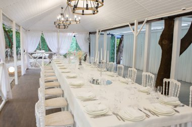 Empty banquet hall ready to receive guests on the summer terrace. white festive table
