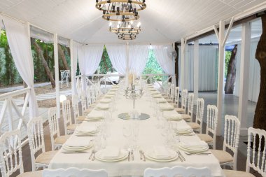 Empty banquet hall ready to receive guests on the summer terrace. white festive table