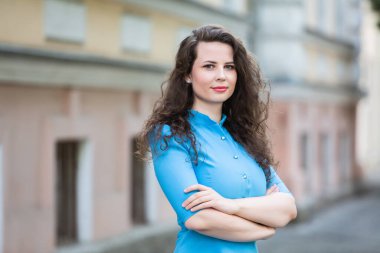 Portrait of a beautiful white European brunette girl wearing a blue dress on the street in the summer.