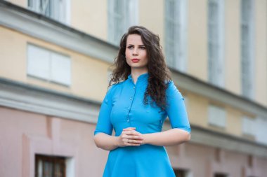 Portrait of a beautiful white European brunette girl wearing a blue dress on the street in the summer.