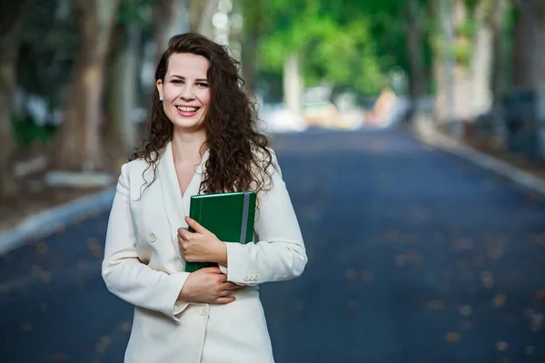 The portrait of a business woman with a notebook in her hand.  Smartly dressed girl outside. Successful white european woman