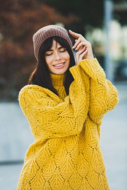 Dışarıda sarı yün kazak ve şapka giymiş güzel bir Avrupalı esmer. Kalın ve şık sonbahar kıyafetleri giyen güzel kız serin havada..