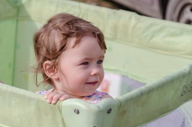 Doğada bir çocuk parkında sarı kıvırcık saçlı, gülümseyen mavi gözlü bir kız..