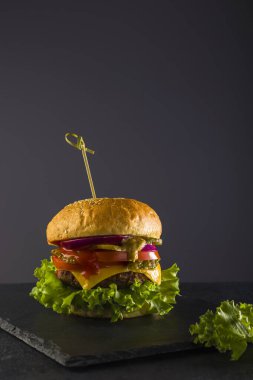 Lezzetli fast food. Tahtadaki siyah arka planda taze sulu burger. Dikey pozisyonda. Boşluğu kopyala