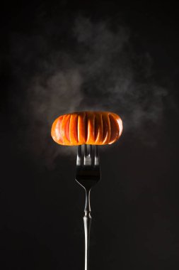 Siyah bir arka planda siyah bir çatalda dumanlı ızgara et sosisi. Kopyalama alanı olan dikey resim.