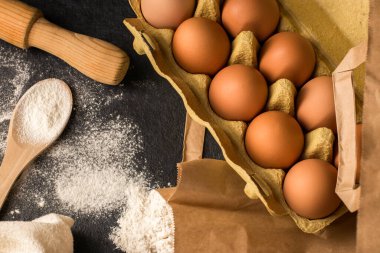 Eko paketinde doğal taze tavuk yumurtası un, siyah mutfak masasında merdane, keten havlu. Pişirmek için geleneksel malzemeler. Üst Manzara. Düz yatıyordu. Kinfolk tarzı