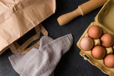 Eko paketinde taze tavuk doğal yumurtası, siyah mutfak masasında merdane, keten havlu. Üst Manzara. Düz plan. Kinfolk tarzı.