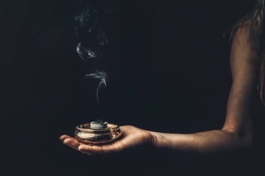 Kadın elinde tütsü, siyah arka planda tütsü dumanı..