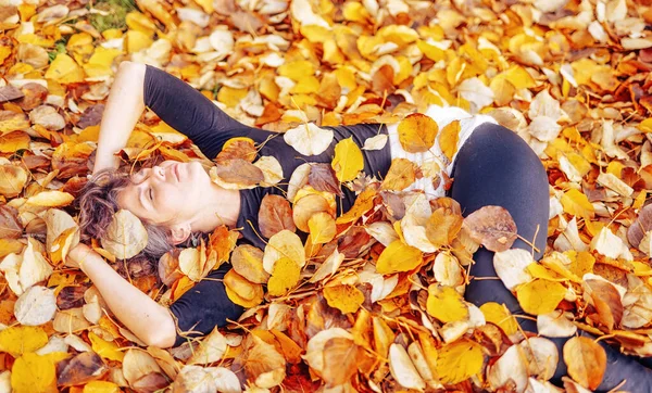 Kadın yaprak yığınına uzanıp oyun oynuyor..