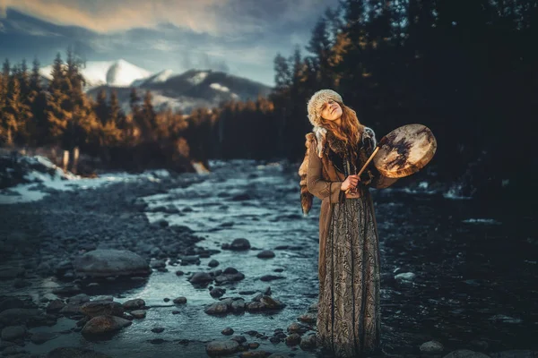 Bela garota xamânica jogando no tambor quadro xamã na natureza. — Fotografia de Stock