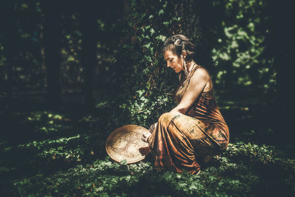 Shamanic woman playing on shaman frame drum in the nature