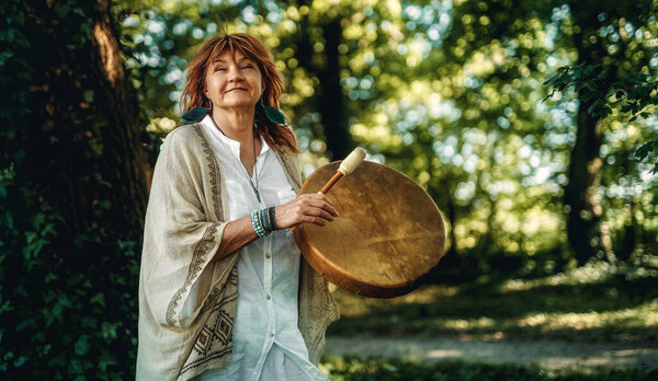 shamanic woman playing on shaman frame drum in the nature