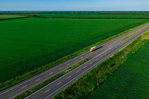 Gele Vrachtwagen Rijden Asfaltweg Langs Groene Velden Scheepvaart Goederen Gezien — Stockfoto