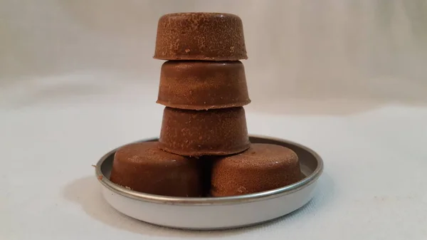 A milk chocolate tower up close. A macro food photography shot of some dark rich sweet chocolate snacks sitting on a small round tin cover.