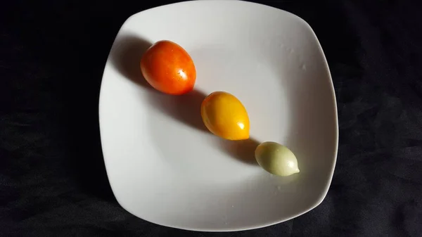 3つの新鮮な選択されたトマトは 小さく 中程度で わずかに大きく白いプレートに斜めに並んでいます トマトは赤または熟しており 黄色または半分熟して緑色です — ストック写真