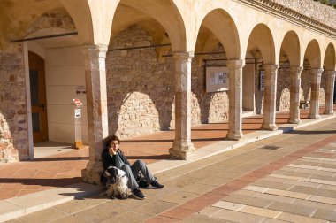 Assisi, İtalya - 20 Kasım 2021, Assisi, İtalya 'da San Francesco Bazilikası önünde köpekli yaşlı bir kadın telefonda konuşuyor.