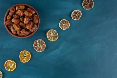Bir kase kurutulmuş hurma ve mavi arka planda limon dilimleri.