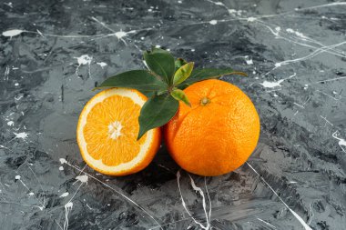 Tam ve dilimlenmiş portakal meyveleri mermer bir zemine yerleştirilmiş.  