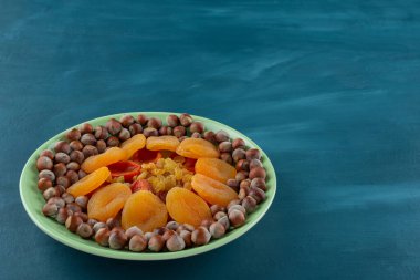 Mavi arka planda yeşil bir tabak kurutulmuş meyve ve fındık. 