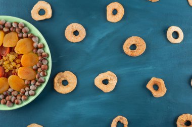 Mavi arka planda yeşil bir tabak kurutulmuş meyve ve fındık. 