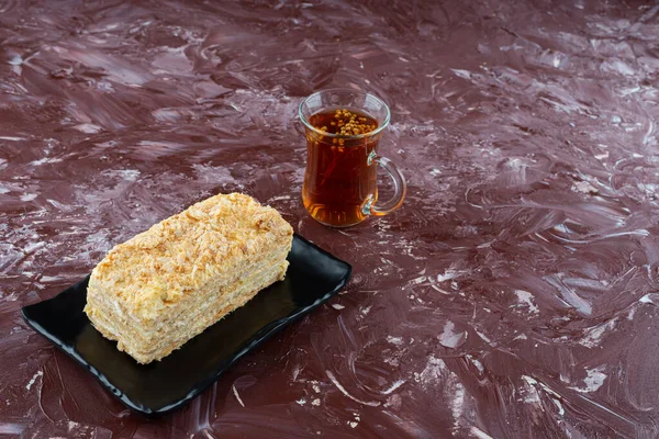 Burgonya arka planında bir tabak dilimlenmiş kek ve bir bardak çay 