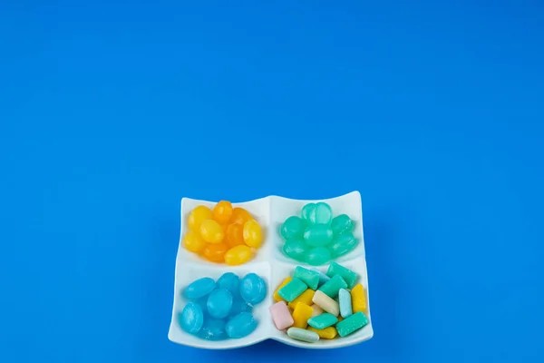 White plate full of hard candies and chewing gums on blue surface