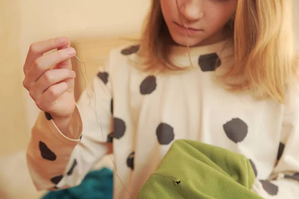 Female child hands hold a needle with a thread and some clothes to mend it. Sustainable consumption, ecology, recycle, sustainability, reusing, concept. — Stockfoto