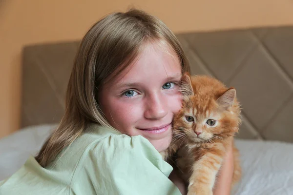 Fille heureuse jouant avec son chat roux sur un lit. Fille aux yeux bleus et chaton. Enfant et animal domestique. — Photo