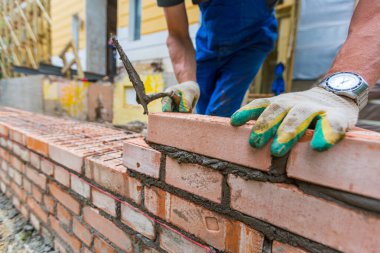 Tuğla ustası inşaat alanında macun bıçağıyla dış duvardaki tuğla işçiliğinin yanında..