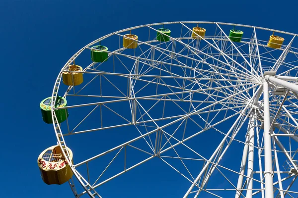 Grande roue blanche avec cabines vertes et jaunes sur ciel bleu — Photo