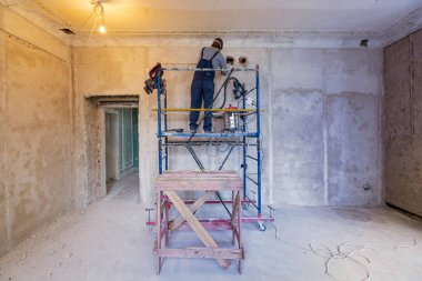 İşçi inşaat, tadilat, yenileme, yenileme, yenileme, restorasyon ve yeniden yapılanma aşamasındaki apartmanın duvarında elektrikli kabil için teknolojik bir delik açıyor..