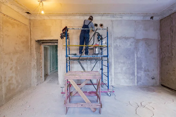 Trabajador está haciendo un agujero tecnológico para el cableado eléctrico en la pared en el apartamento que está en construcción, remodelación, renovación, extensión, restauración y reconstrucción. —  Fotos de Stock